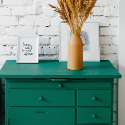 A green drawer, with a two paintings and a plant on top of it