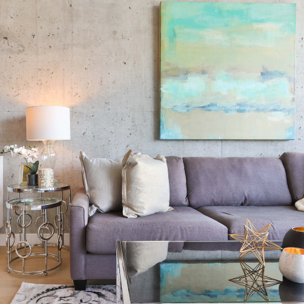 A living room with a grey couch, coffee table, table lamp and a painting on the wall